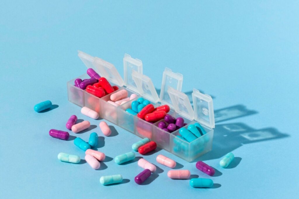 Lijekovi različitih boja u kutijici za lijekove i oko nje